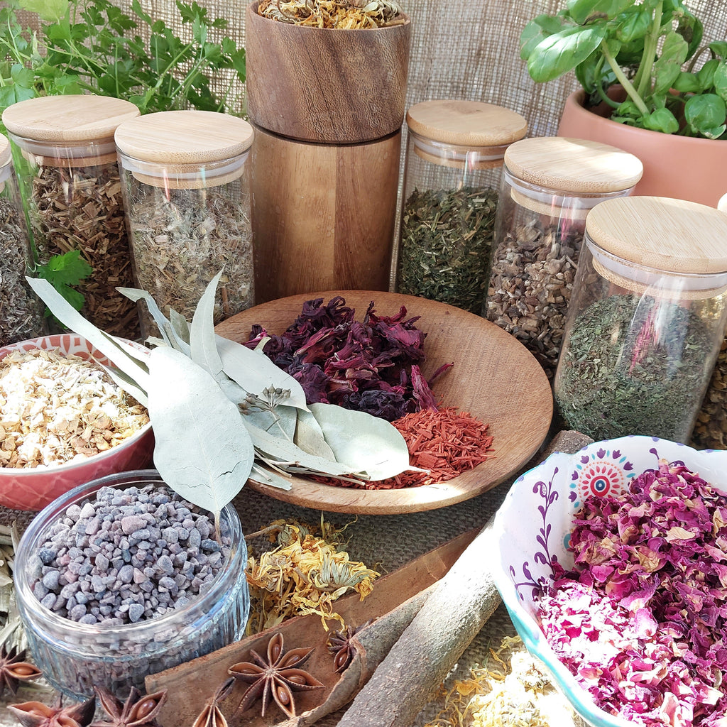 Assorted herbs and spices in glass jars and bowls on a wooden surface.