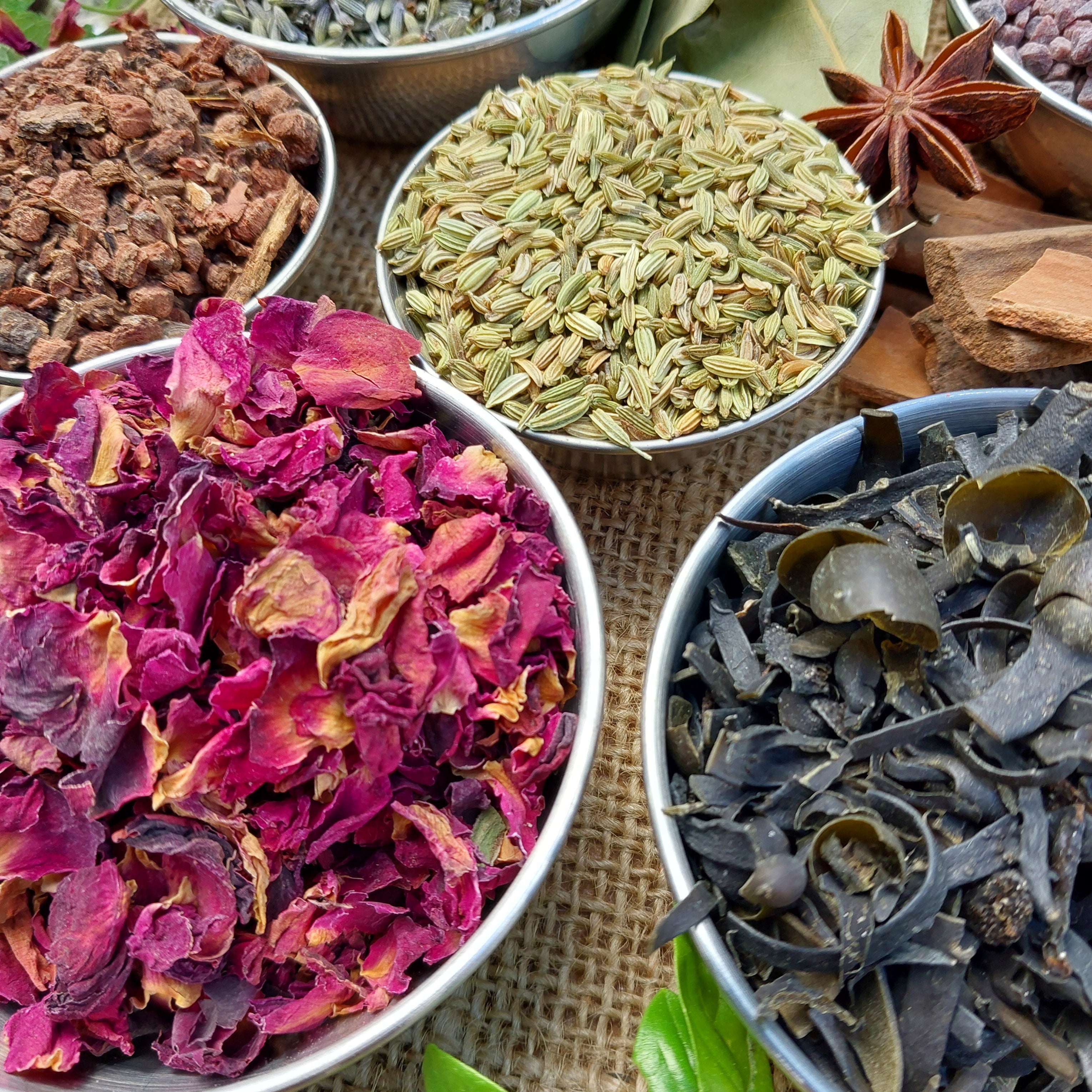 Assorted dried herbs and spices in small bowls on a textured surface.